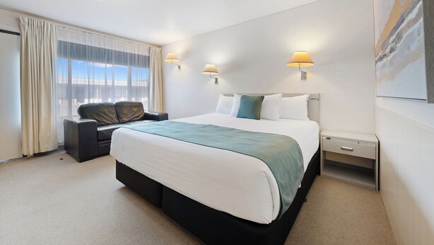 A hotel room with a large bed, a sofa, a nightstand, and a window with curtains. - Comfort Inn Devonport (Devonport)