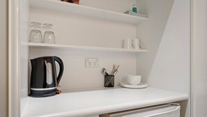 A kitchenette with a white countertop, a coffee maker, a kettle, a dish rack, and a small refrigerator. - Comfort Inn Devonport (Devonport)