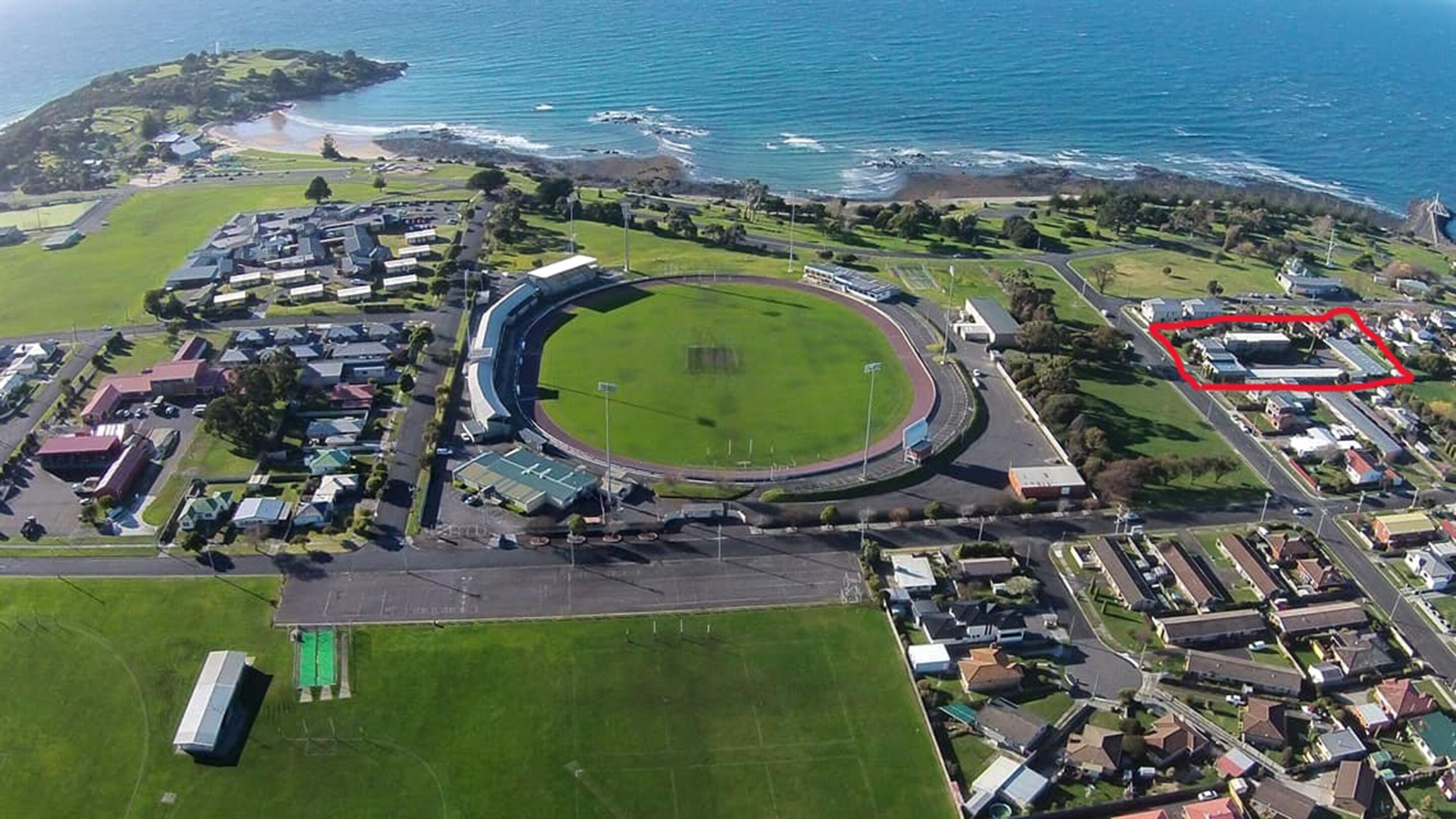 Vista aérea de un estadio con pista circular, rodeado de edificios residenciales y una playa.