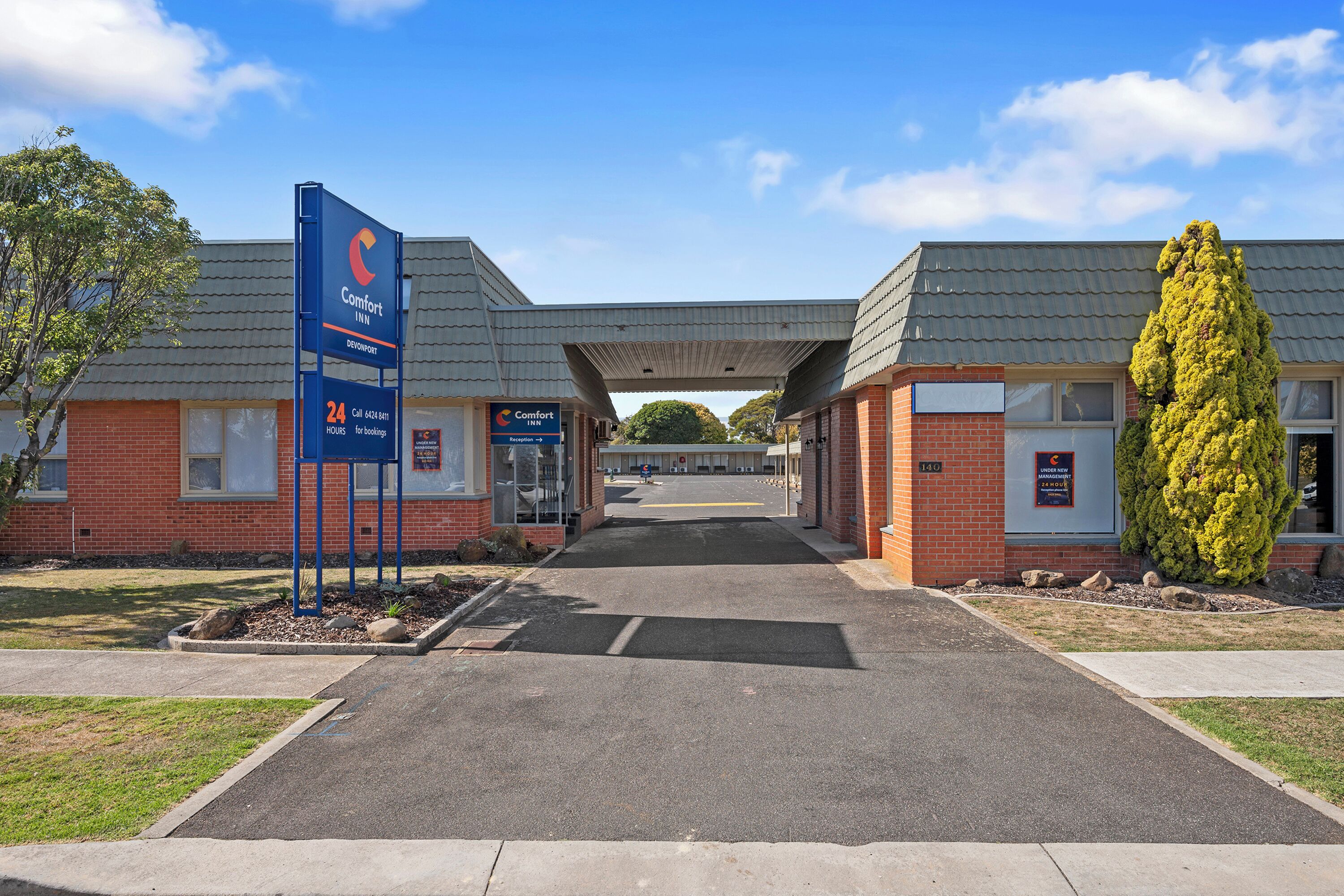 A Comfort Inn hotel entrance with a clear sky, a signboard, and a well-maintained lawn.