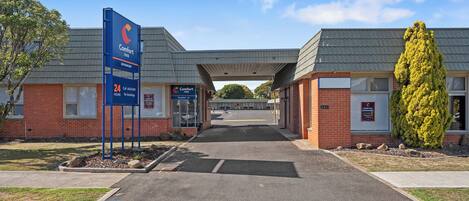 A Comfort Inn hotel entrance with a clear sky, a signboard, and a well-maintained lawn.