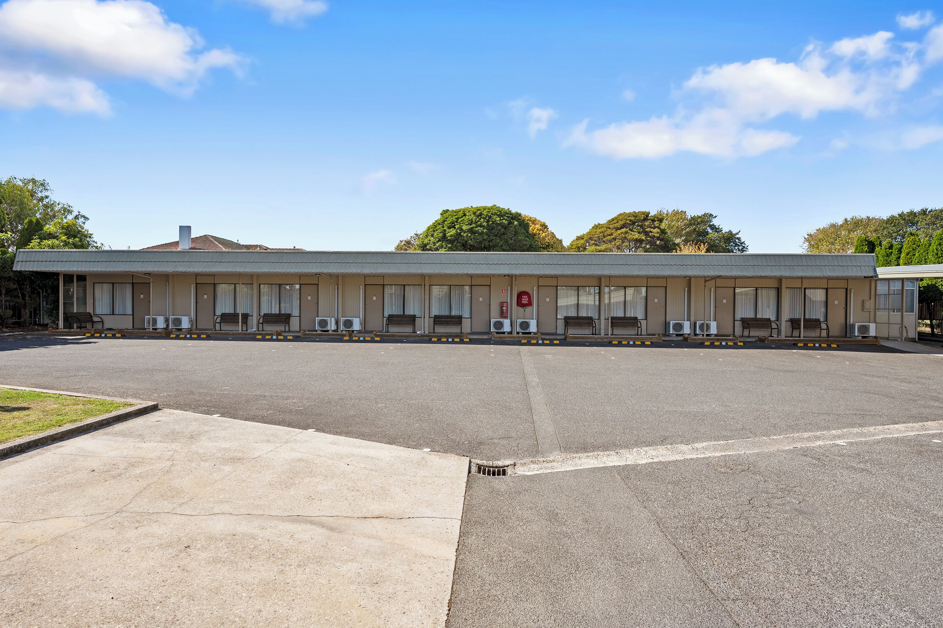 Un motel con una hilera de habitaciones, un estacionamiento y cielo despejado.