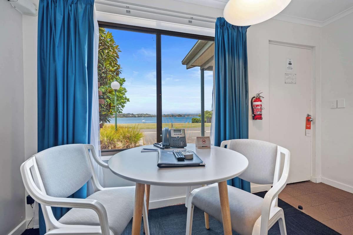 A room with a round table, two chairs, a phone, a notepad, and a pen. A fire extinguisher is mounted on the wall.