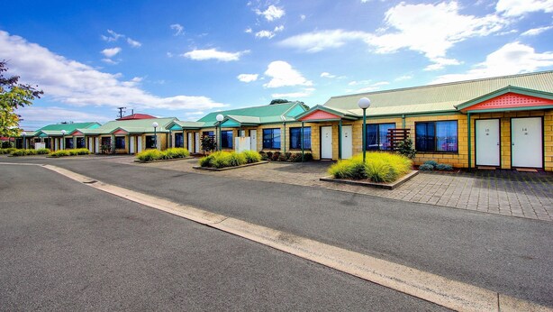 A row of motel buildings with green roofs and a paved parking area.