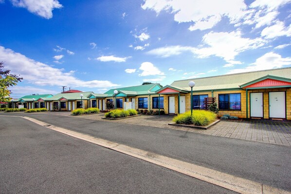 A row of motel buildings with green roofs and a paved parking area.