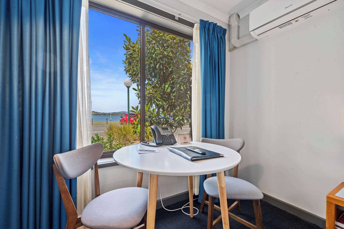 A room with a round table, two chairs, a telephone, and a window with curtains.