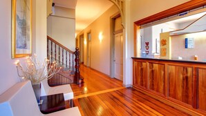 A hallway with wooden flooring, a staircase with a wooden railing, and a reception desk with a wooden counter. - Comfort Inn The Pier (George Town)