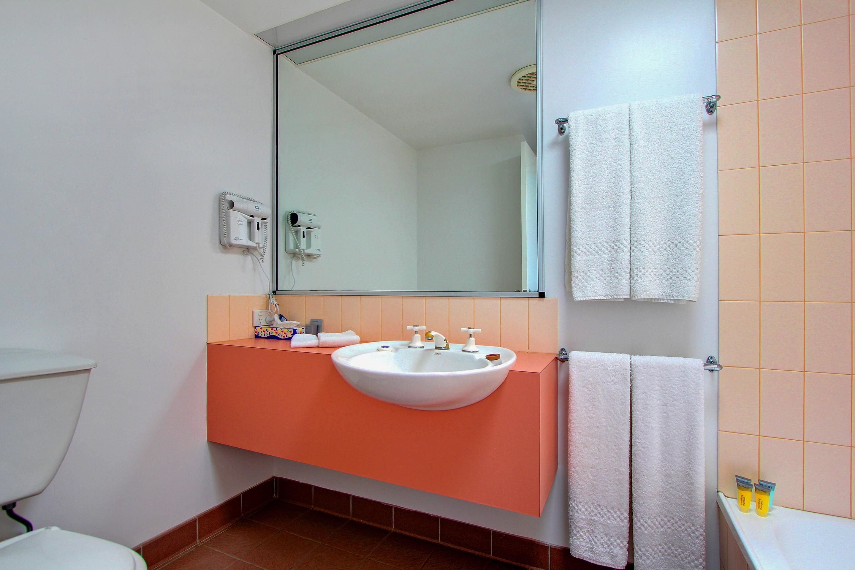 Un baño con lavamanos blanco, encimera naranja y espejo sobre el lavamanos.