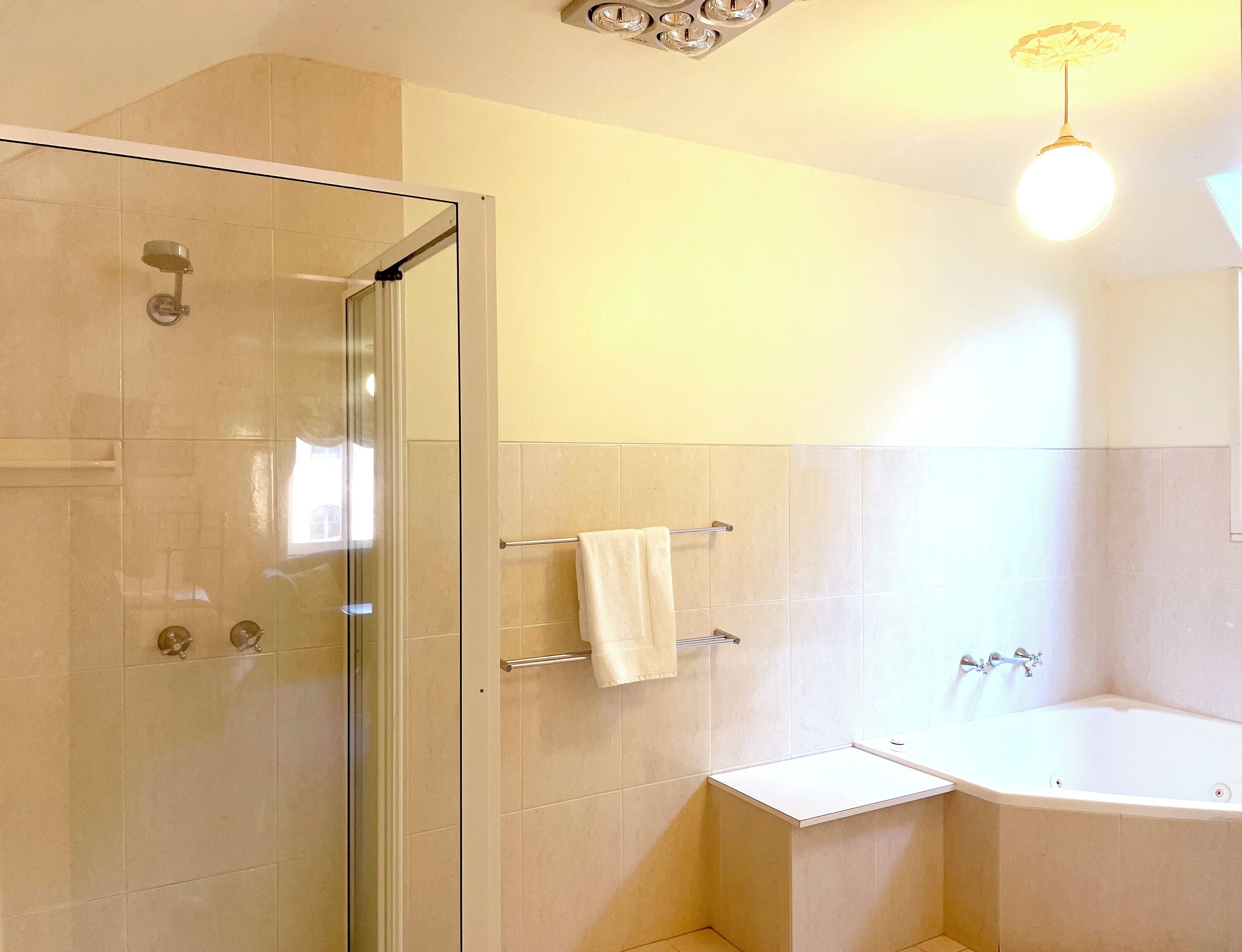 Une salle de bain avec une douche à parois de verre, une baignoire blanche et un petit meuble-lavabo doté d’un porte-serviettes.