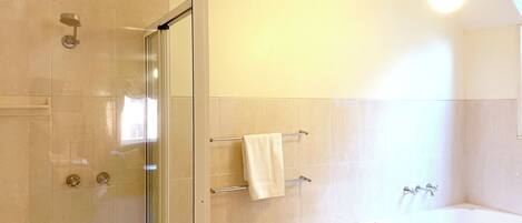 A bathroom with a glass-enclosed shower, a white bathtub, and a small vanity with a towel rack.
