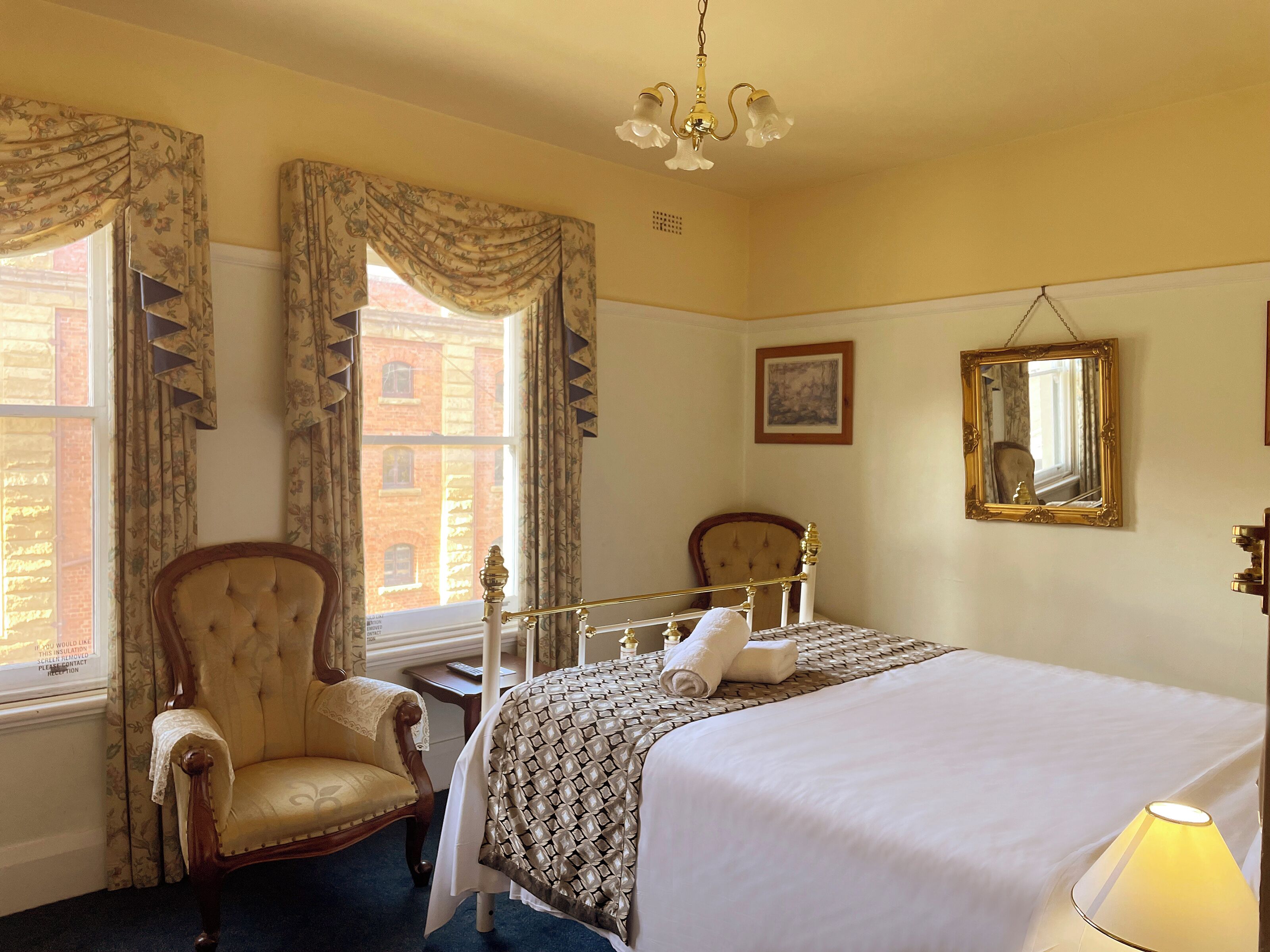 A hotel room with a bed, a chair, a bedside table, a lamp, and a window with curtains.