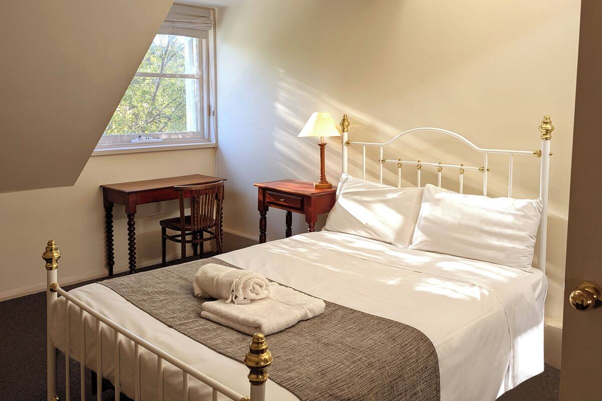 A bedroom with a bed, a nightstand, a chair, a window, and a door.