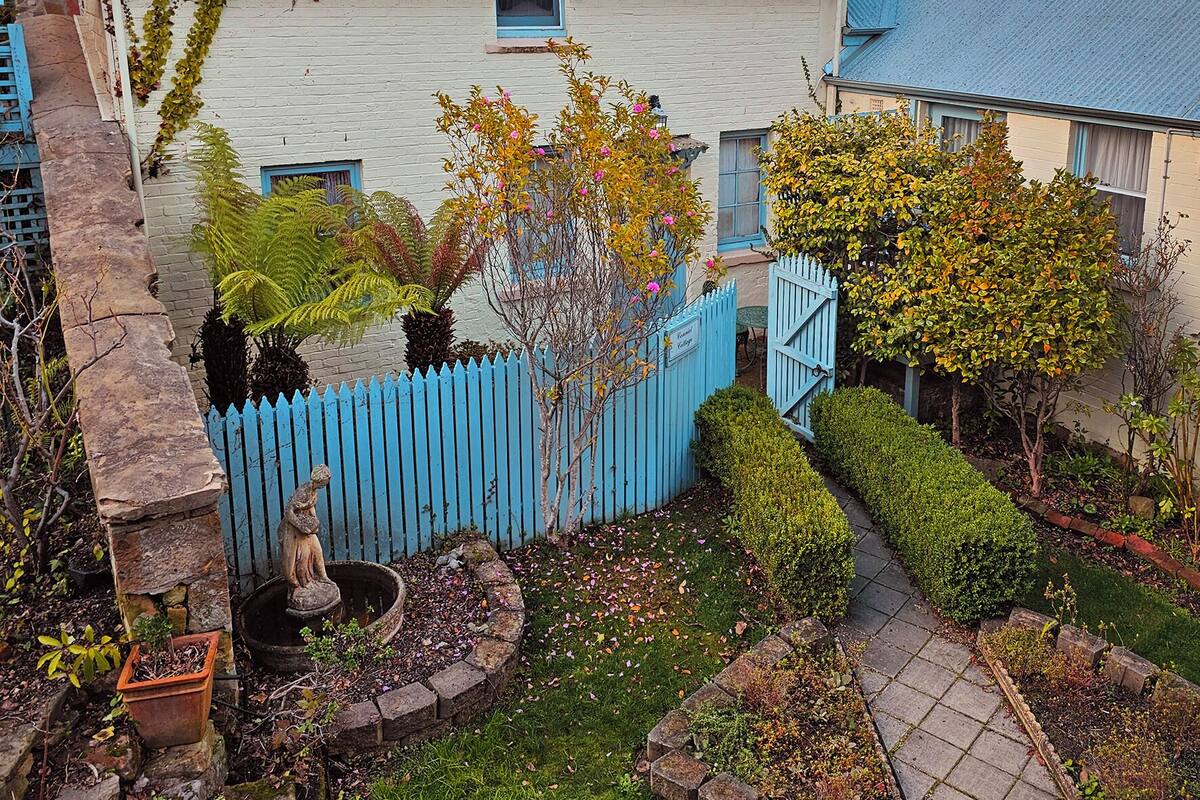 A residential property with a blue picket fence, a garden with various plants and a small statue, and a house with a blue roof and white walls.