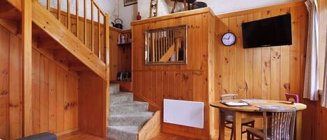 Un intérieur en bois comprenant un escalier, un coin repas et un téléviseur fixé au mur.