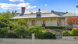 A two-story house with a gabled roof, a chimney, and a small attached garage. - The Lodge on Elizabeth (North Hobart)