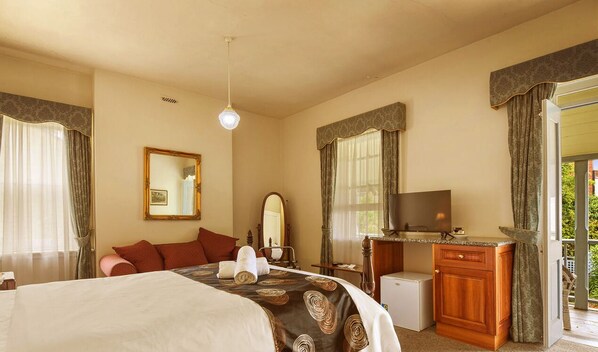 A hotel room with a bed, a desk with a television, a mirror, and a small refrigerator. - The Lodge on Elizabeth (North Hobart)