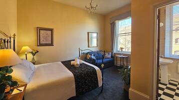 Ett hotellrum med två sängar, en kristallkrona, en soffa, ett litet bord med en vas och utsikt över staden genom fönstret.