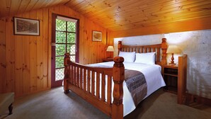 A wooden-paneled bedroom with a bed, a nightstand, a lamp, and a window with a view of greenery. - The Lodge on Elizabeth (North Hobart)