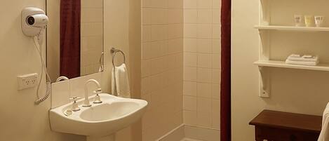 A bathroom with a sink, mirror, shower, and a small wooden shelf with toiletries.