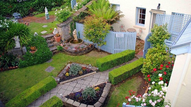 A well-maintained garden with a fountain, neatly trimmed hedges, and a variety of plants. - The Lodge on Elizabeth (North Hobart)