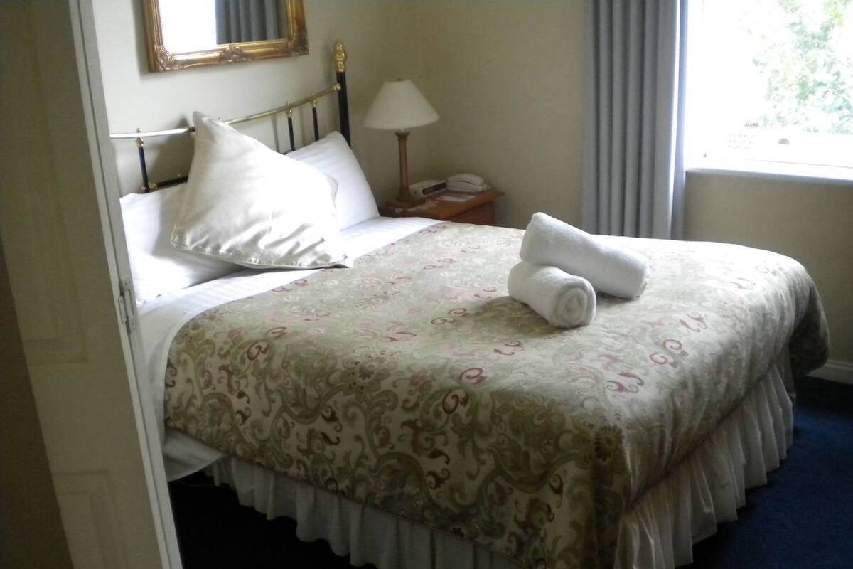 A neatly made bed with a patterned bedspread, a bedside lamp, and a nightstand with a telephone.