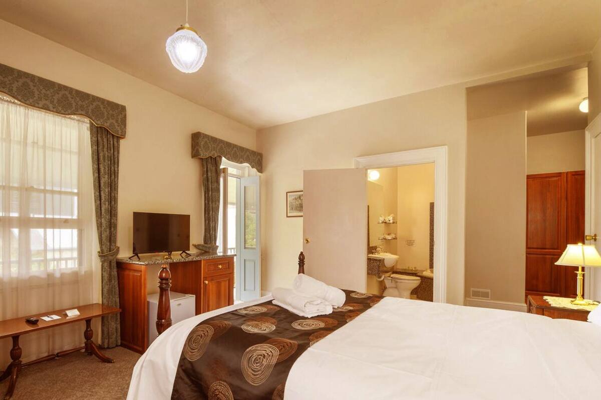 A hotel room with a large bed, a desk with a chair, a vanity with a mirror, and a bathroom with a toilet and sink.
