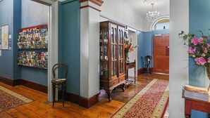 A hallway with a wooden floor, a bookcase filled with books, a chair, and a vase with flowers. - The Lodge on Elizabeth (North Hobart)