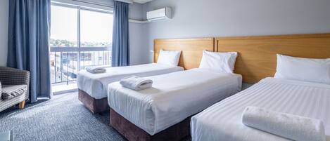 A hotel room with two beds, a sofa, a large window with curtains, and an air conditioning unit.