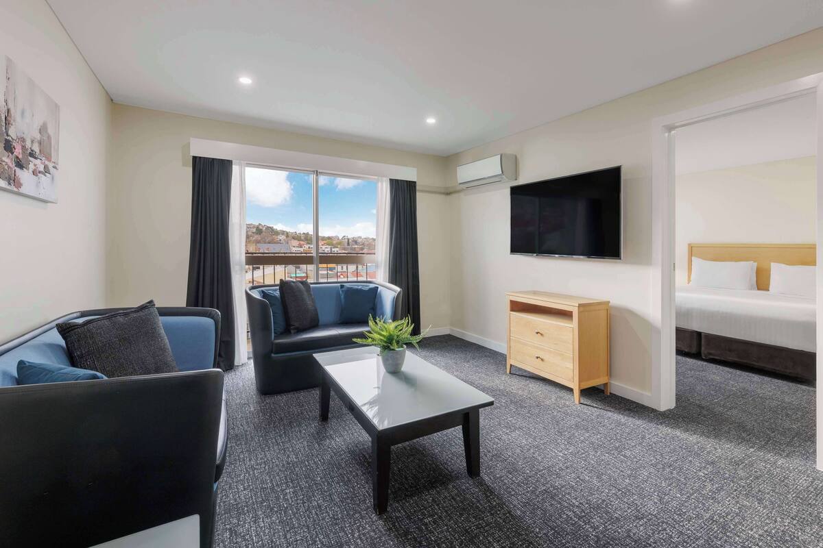 Quarto de hotel moderno com varanda, televisão de tela plana, cama, sofá, mesa de centro e escrivaninha.
