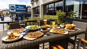 An outdoor dining area with wicker furniture and a variety of dishes including pizzas, salads, and burgers. - Best Western Hobart (Hobart)