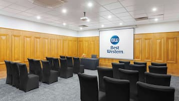 A conference room with rows of black chairs, a projector screen displaying "BW Best Western," and wooden paneling on the walls.