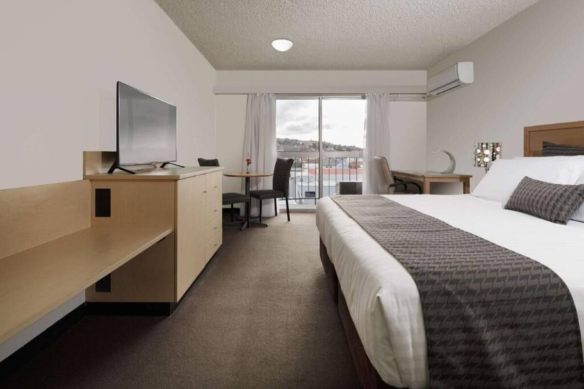 Quarto de hotel com cama, escrivaninha, cadeira, televisão e vista para o exterior.