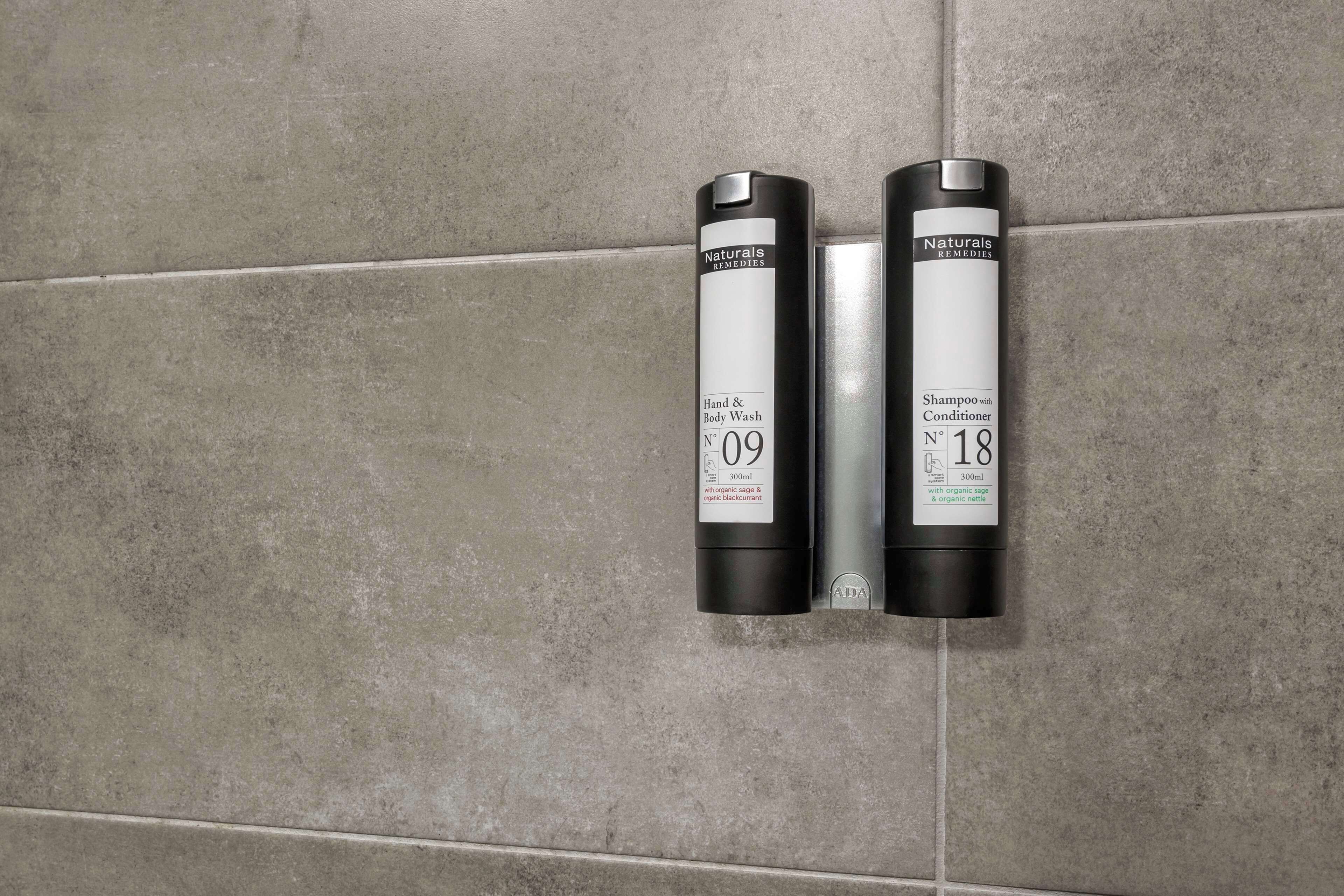 Two bottles of hand and body wash on a tiled wall.