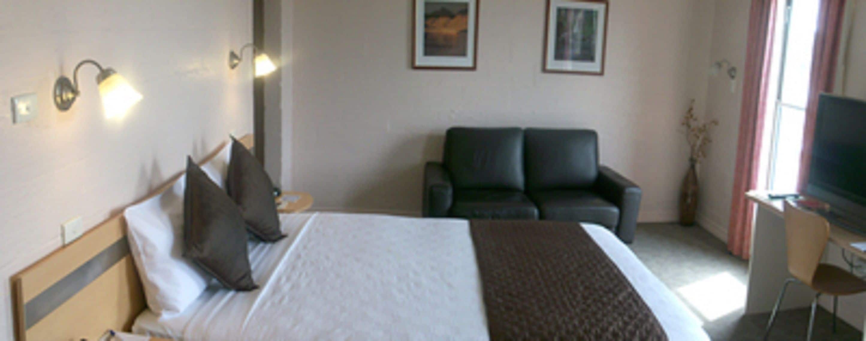 A hotel room with a bed, a desk, a chair, a sofa, and two wall-mounted lamps.
