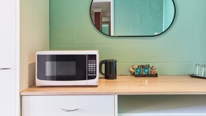 A microwave on a wooden countertop with a green wall and a mirror above it. - Balmoral On York (Launceston)