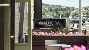 A sign for 'Balmoral on York' with a view of a hillside and a patio area with chairs and tables. - Balmoral On York (Launceston)