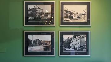 Una habitación con una pared verde, cuatro fotografías blanco y negro, una araña y dos mesas redondas con sillas.