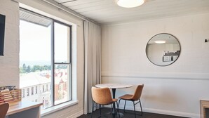A hotel room with a large window, a round mirror, a round table with two chairs, and a bed. - Balmoral On York (Launceston)
