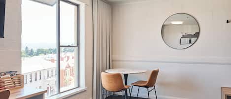 Una habitación de hotel con un ventanal grande, un espejo redondo, una mesa circular y dos sillas, además de una cama.