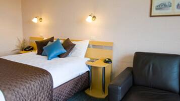 A hotel room with a bed, a bedside table with a lamp, a chair, and a wall-mounted phone.