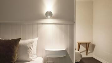 Un dormitorio con una cama, una mesita de noche, una lámpara de pared y un taburete de madera.