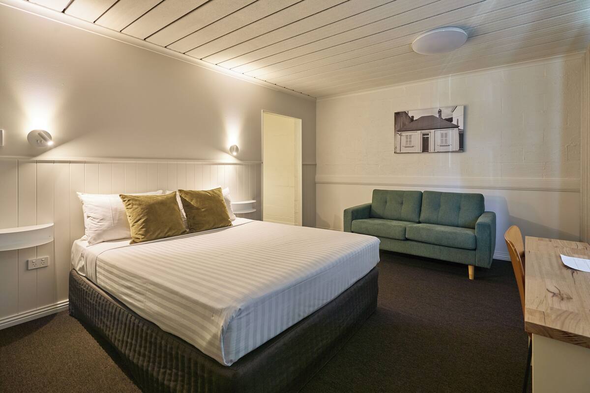 A bedroom with a bed, a green sofa, a wooden table, and a wall-mounted picture.