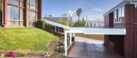 A hotel with a covered entrance, a grassy lawn, and a view of a cityscape in the background.