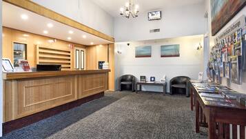A reception area with a wooden reception desk, a computer, a small table with brochures, two chairs, and a carpeted floor.