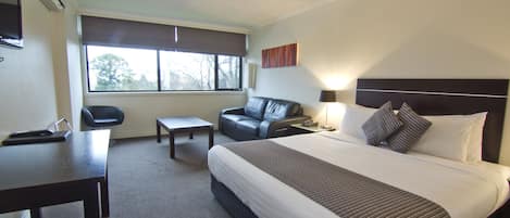 Habitación de hotel con una cama grande, un escritorio, una silla, un sofá y una ventana con vistas a árboles.