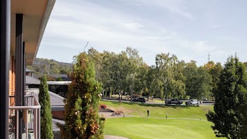 Vista de un campo de golf con una persona jugando, rodeado de árboles y coches aparcados.