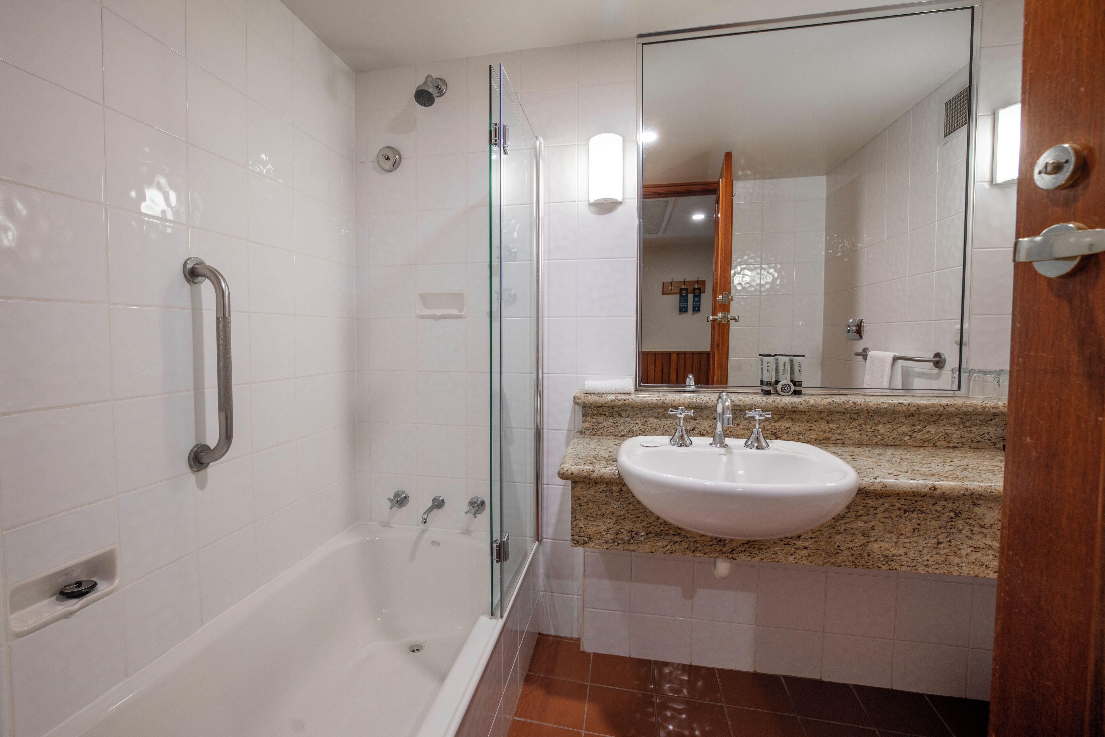 A modern bathroom with a glass-enclosed shower, a white bathtub, and a granite countertop sink.