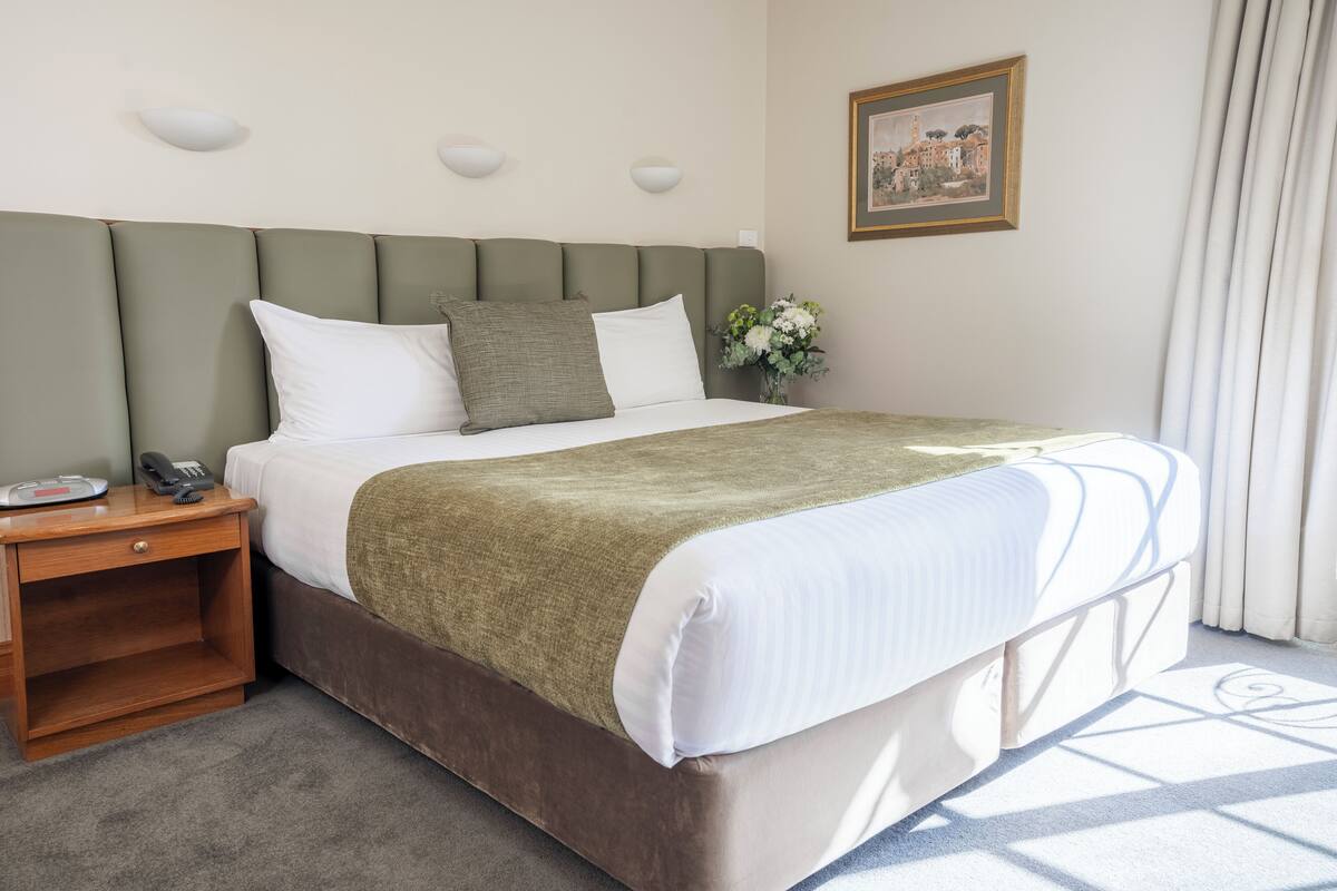 A neatly made bed with a green headboard, white bedding, and a bedside table with a telephone.