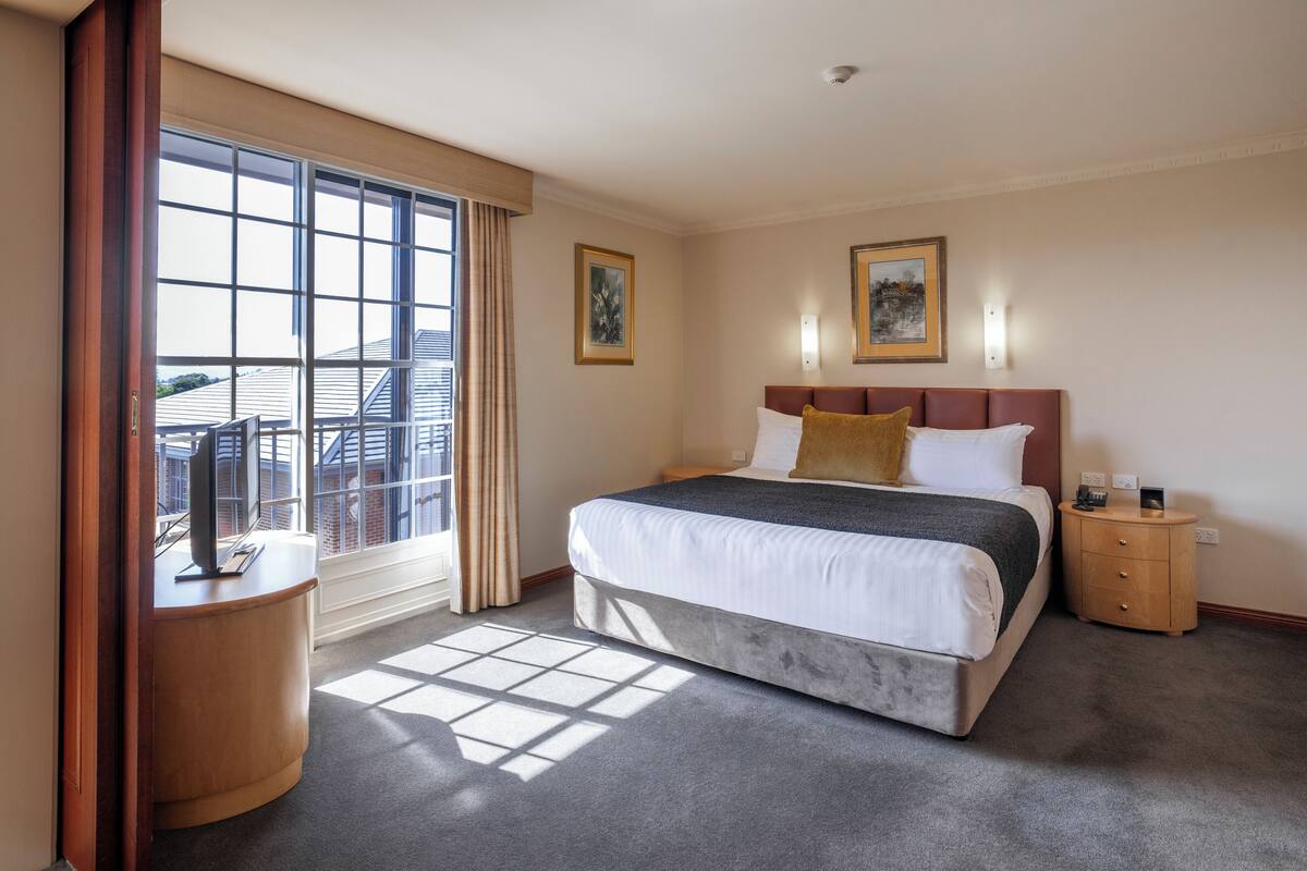 A hotel room with a large bed, a nightstand, a desk, and a window with curtains.