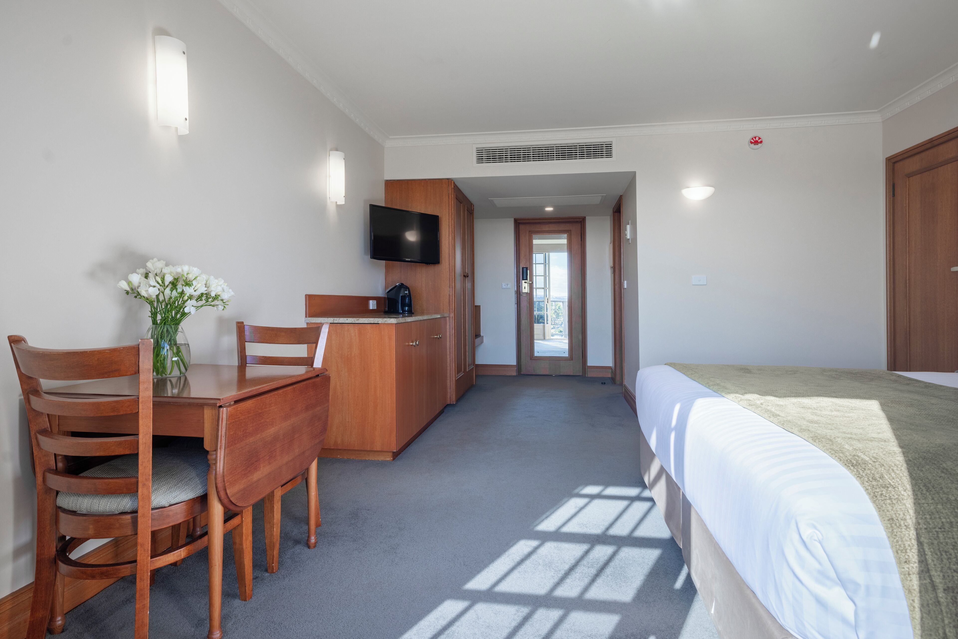 A hotel room with a bed, a desk with a chair, a television, and a door leading to a balcony.
